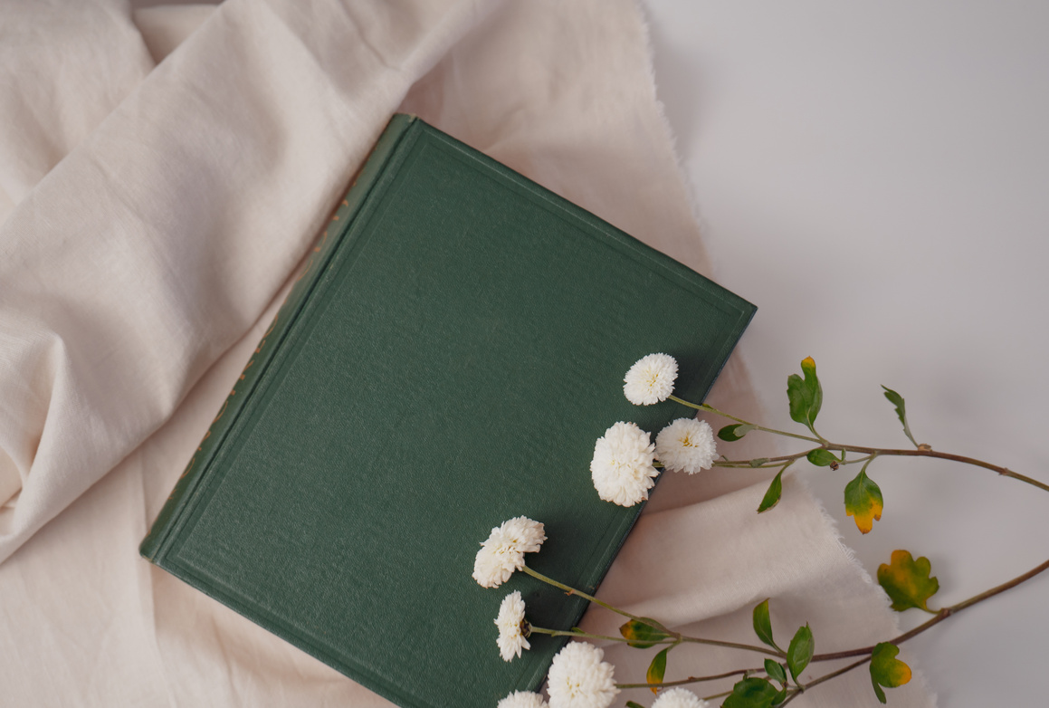A green hardcover journal with fresh white flowers placed on the right hand side of it, slightly hovering over the cover.